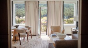 A view from floor-to-ceiling windows framed by cream curtains in a guest room overlooks the Swiss mountains
