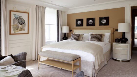 double bed in hotel guestroom alongside window with textiles and wallcovering in contemporary neutrals