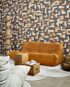 brown slouch couch and wooden totem in front of abstract wallpaper design