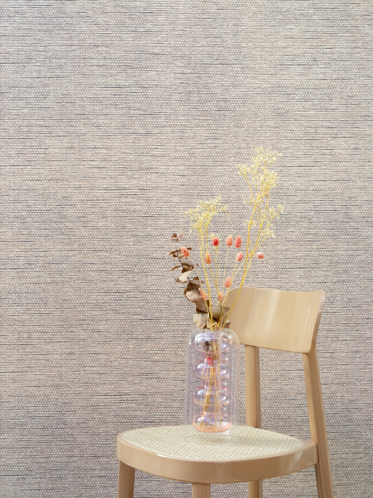 single wooden chair with dried flowers in front of textured woven wall covering