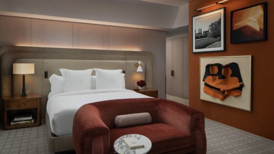burnt orange sofa at foot of the bed in Four Seasons New York guestroom with low lighting and art on the wall