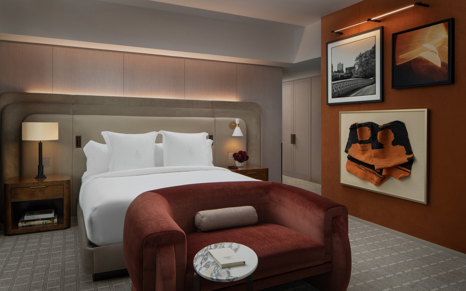 burnt orange sofa at foot of the bed in Four Seasons New York guestroom with low lighting and art on the wall