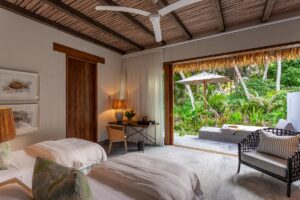 Seychelles villa accommodation with doors in front of bed opening to deck and palm trees