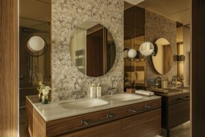 ensuite guest bathroom with wooden vanity and round mirror on neutral floral wall above basin