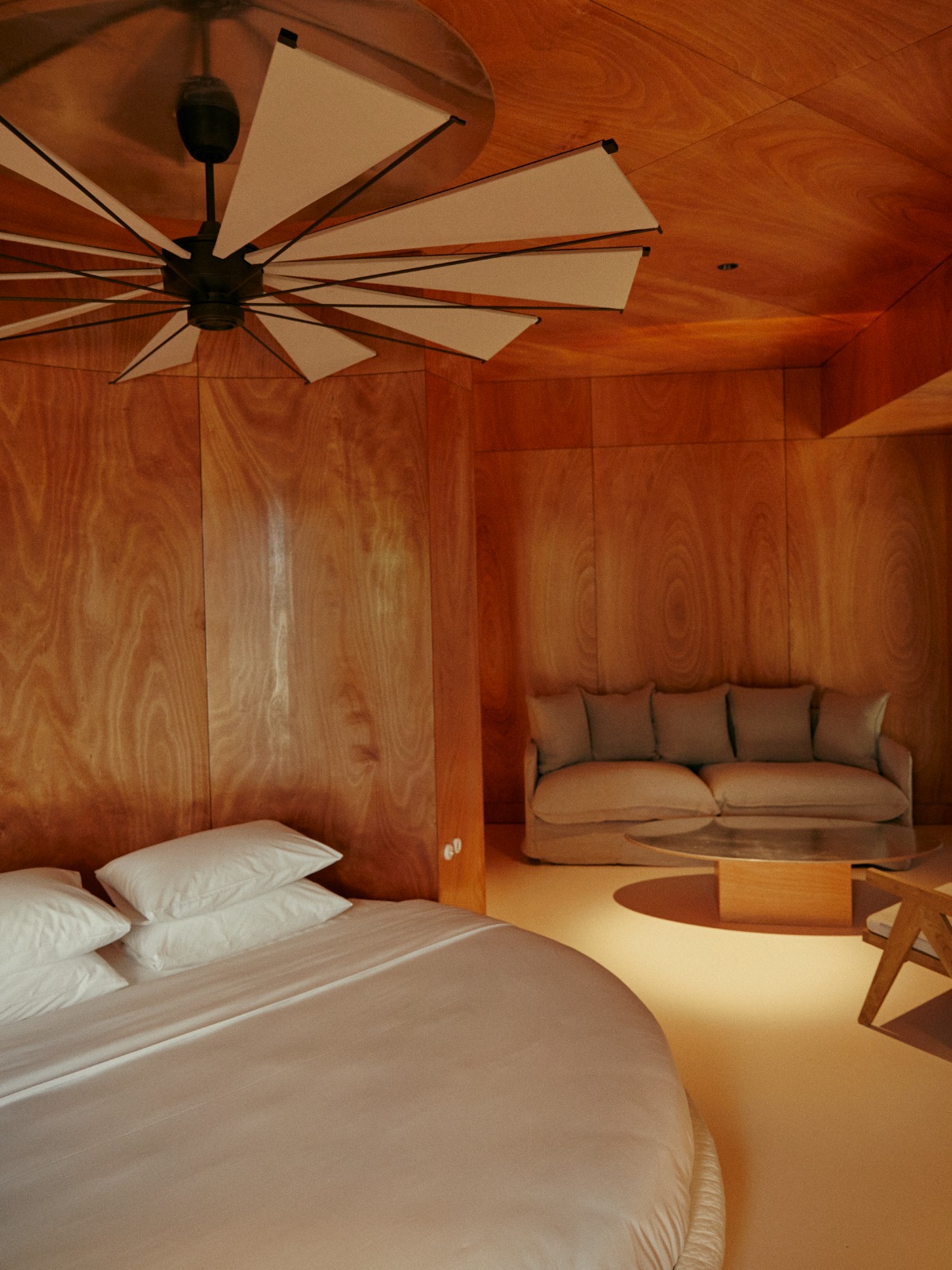 round bed below ceiling fan in guestroom with wood panelled walls