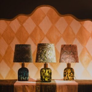 three glass lampbases with painted shades in front of harlequin backdrop