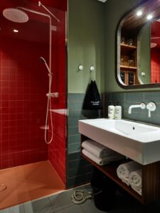 bathroom with orange shower enclosure, green walls and tiles and white Bette fittings