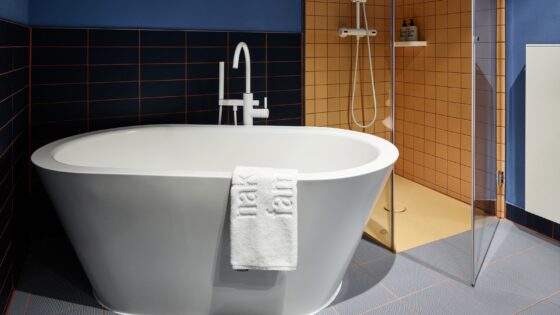 Freestanding Bette bath in 25hours bathroom with yellow shower cubicle and blue walls