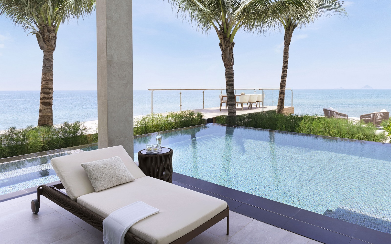 white sun lounger next to pool in front of palm trees and beach at Gran Meliá Nha Trang