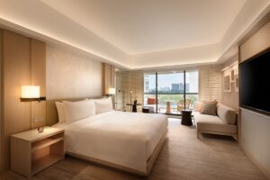 double bed with white linen in guestroom with natural tones and textures and view over Singapore