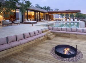 cushioned seating around fire pit on wooden deck next to swimming pool at safari lodge