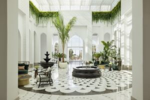hotel lobby with hanging plants and palm trees above patterned marble floor and fountain
