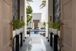 entrance through wooden doors into courtyard with plants and swimming pool at Raffles Al Areen Palace Bahrain