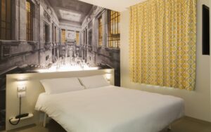 hotel guestroom in Milan with yellow curtain and mural behind the bed