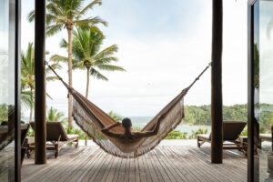 person in hammock looking out at palm trees and beach
