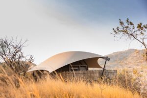 curved canvas tented roof over wood and brick structure surrounded by grasslands