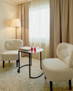 guestroom window corner with white chairs, art deco table and cream curtains