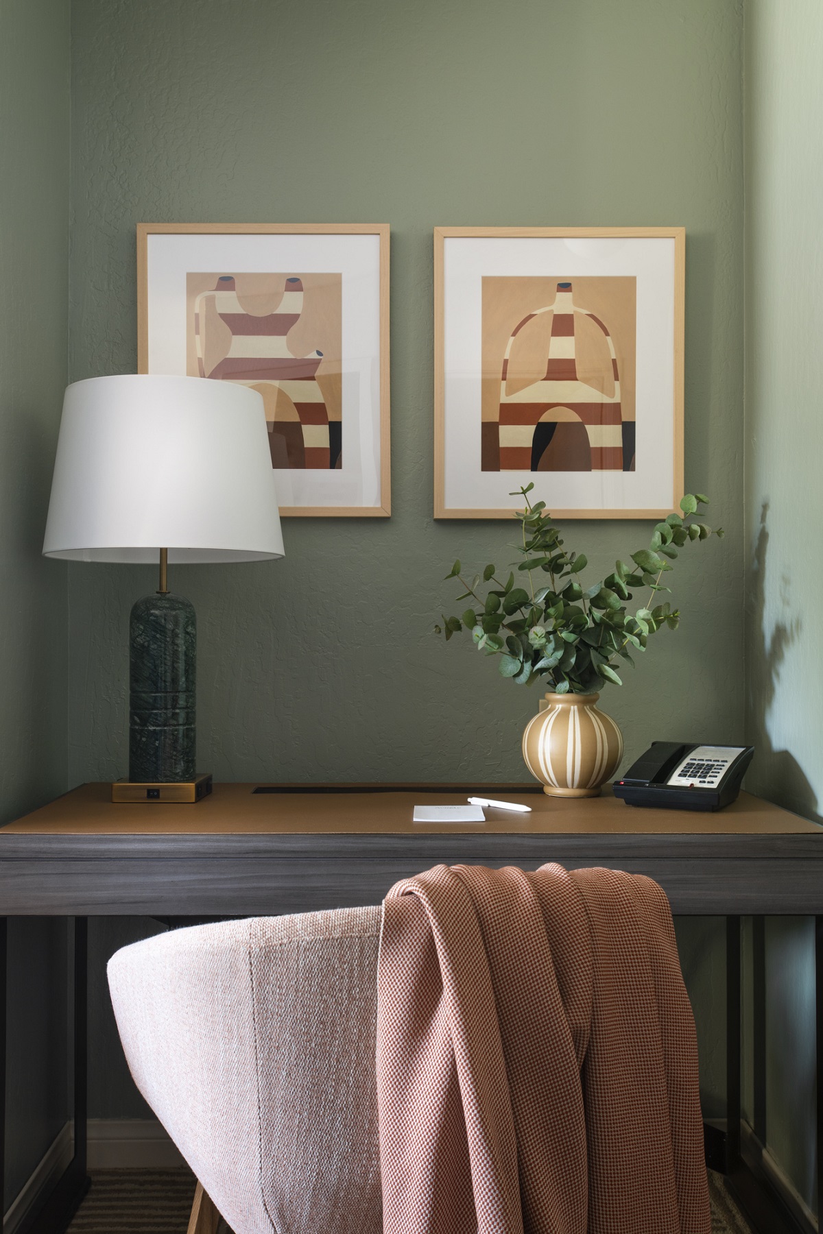 guestroom corner with chair and desk with art work on sage green wall