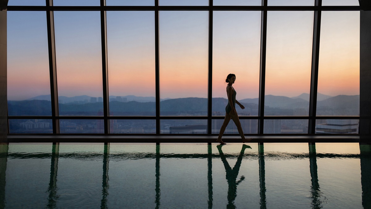 A woman walks the length of the 38th-floor indoor pool with views of the mountains at sunset. 