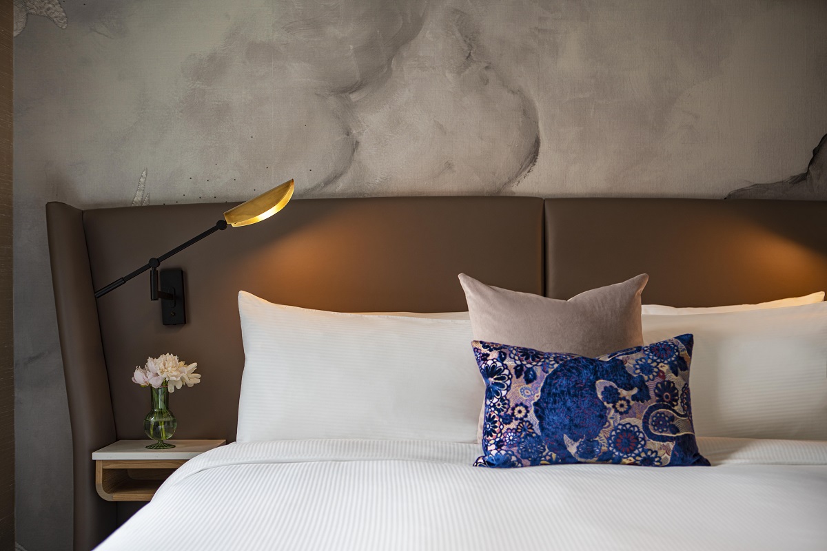 detail of bed in suite with headboard and light with blue cushion on white linen