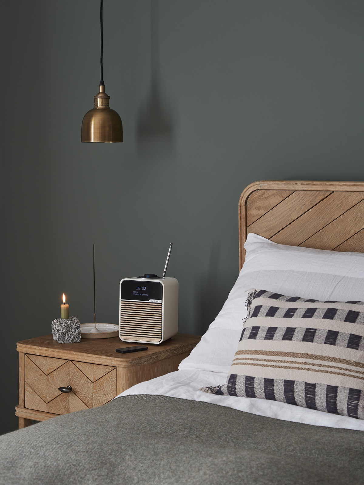 wooden bed with patterned cushion and grey throw with Ruark radio on table