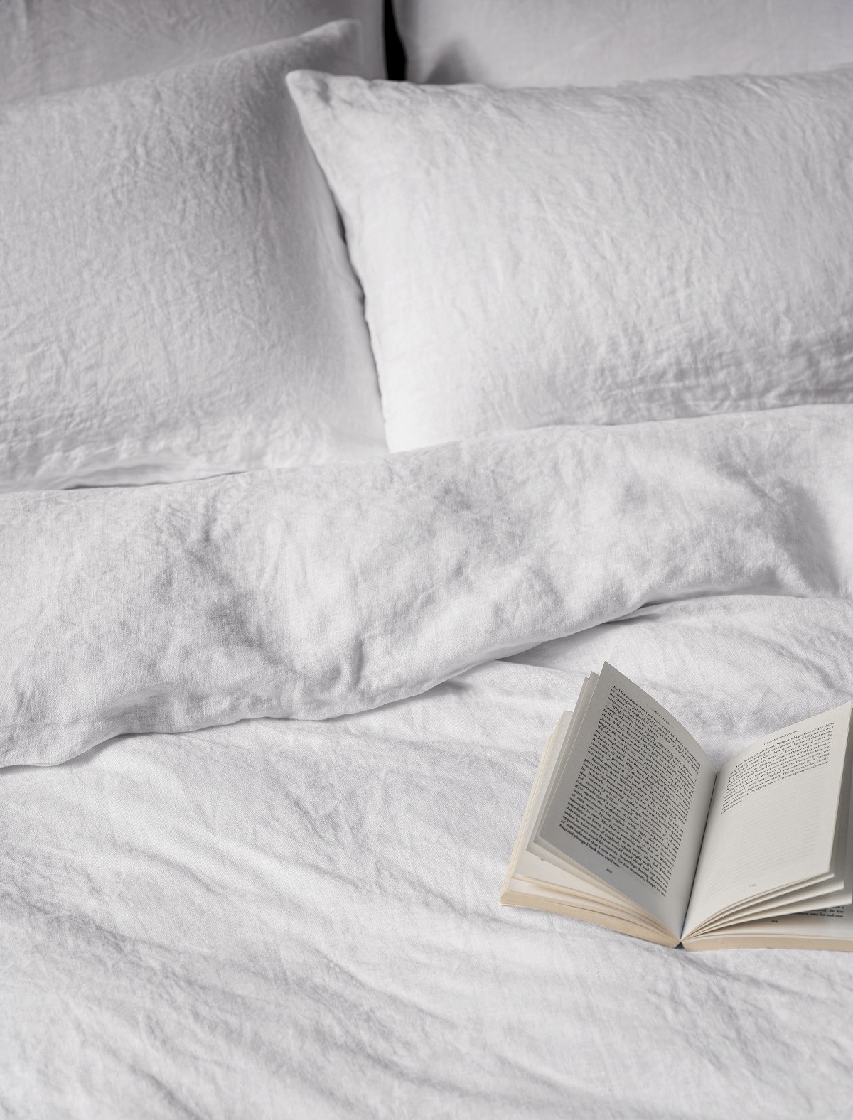 detail of washed organic linen sheets rumpled on bed with open book