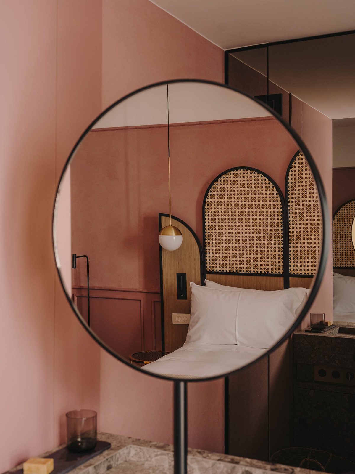 round mirror in bedroom reflecting plaster pink walls and rattan headboard
