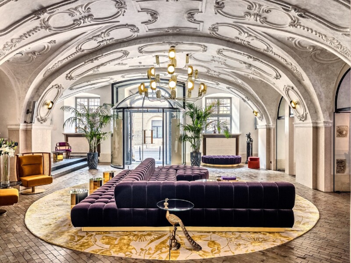 An opulent lobby space with ornate curved ceilings, brick floor, and oversized deep purple lounge seating. 