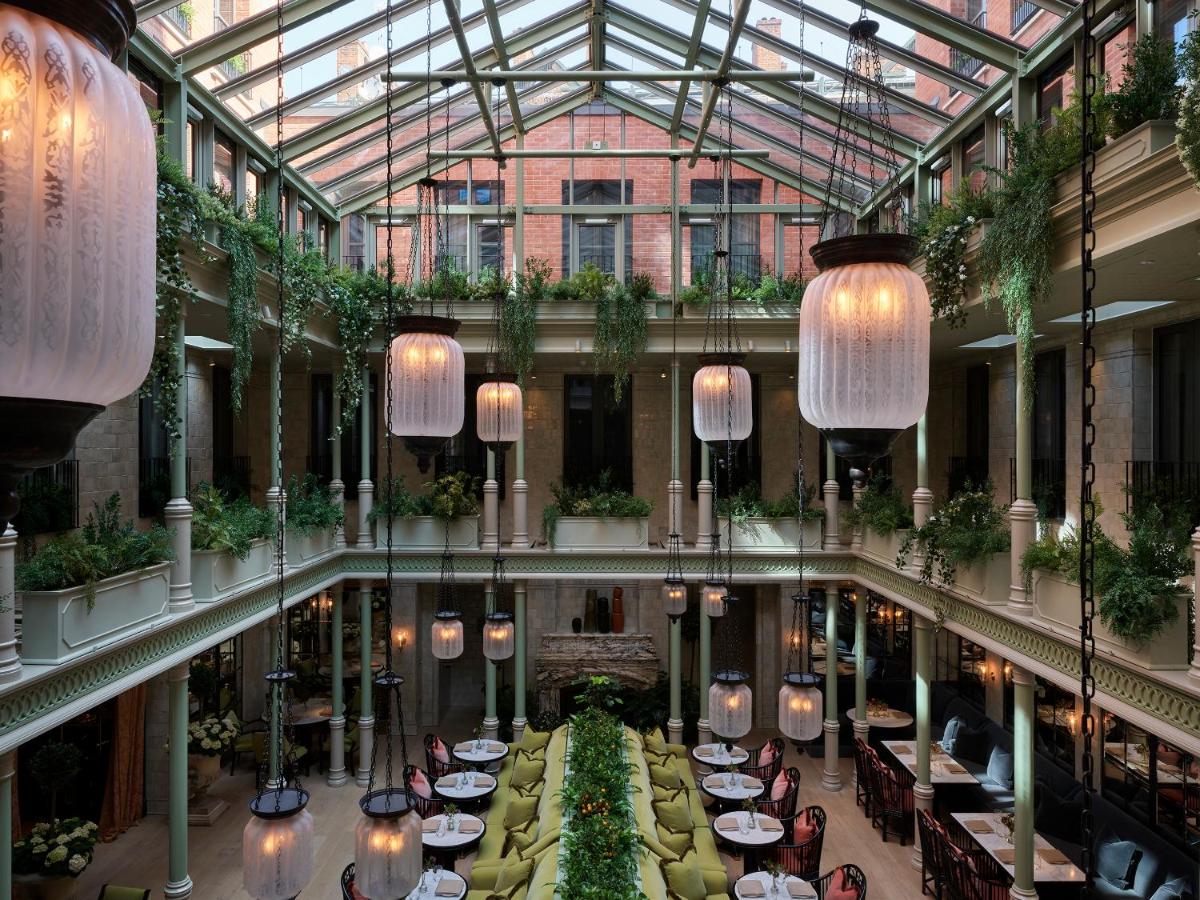 Suspended glass lanterns hang from the triple-height atrium of the NoMad's main restaurant. Vibrant green foliage frames each balcony level with the dining area centrally on the ground floor. 