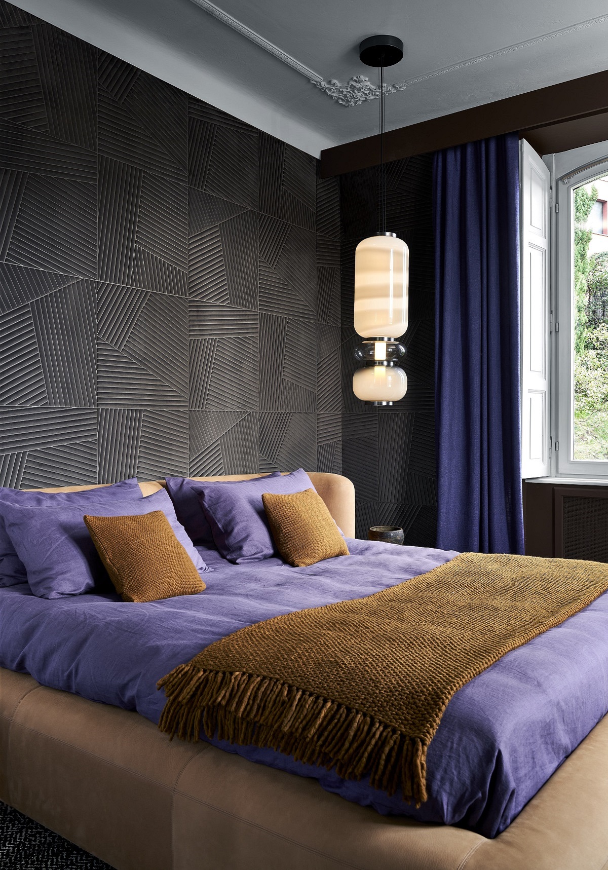 dark grey wall with brown and purple bed covering and statement light above bed