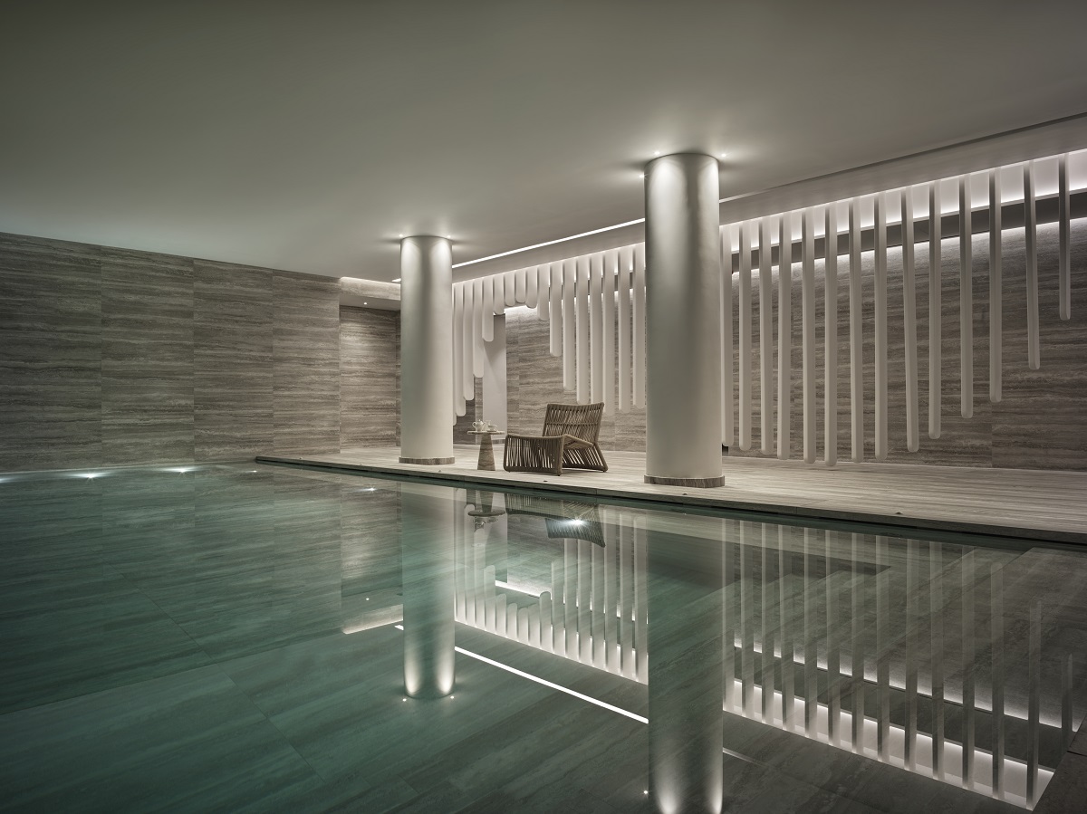 A luxurious indoor pool framed by neutral-toned tiled walls and stone columns. 