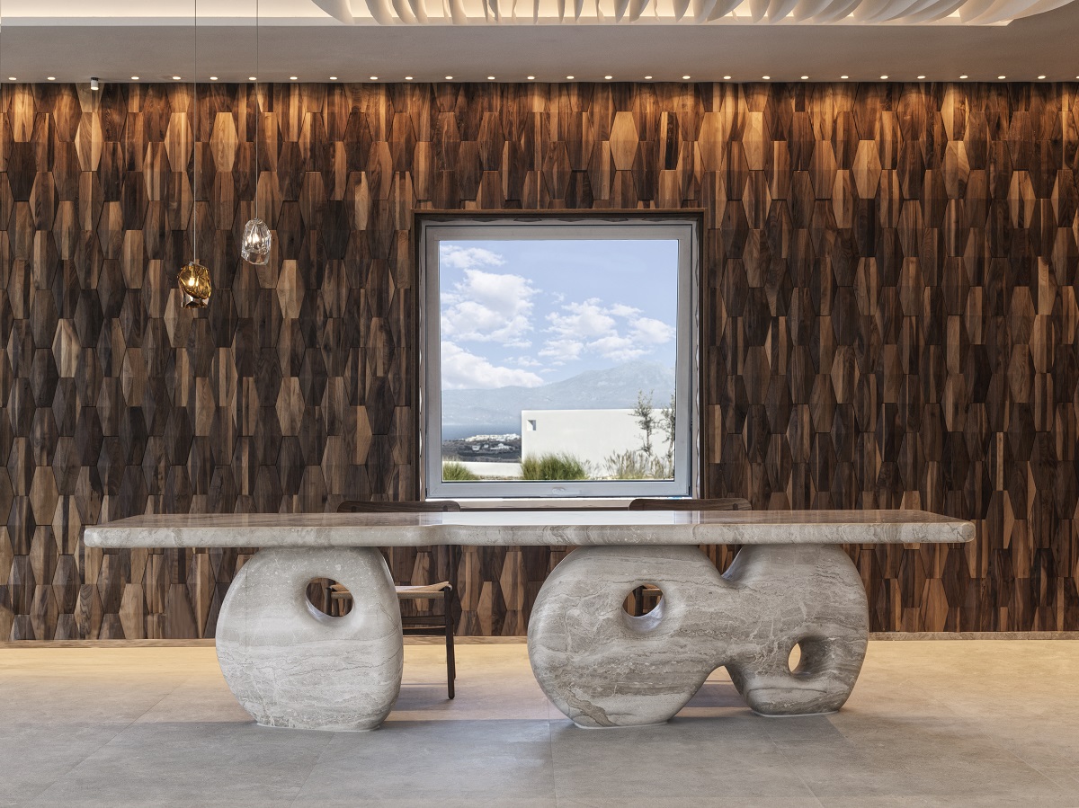 A reception desk made of grey and white veined marble combines curves and straight lines with a backdrop of floor-to-ceiling mutli-tonal wood and a central window overlooking Mykonos.