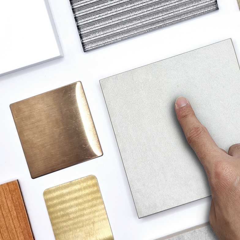 architect's hand pointing to samples of interior material in top view containing grey stone tiles, green velvet drapery, wooden veneer, corrugated glass, white quartz, aluminum plate for selection.