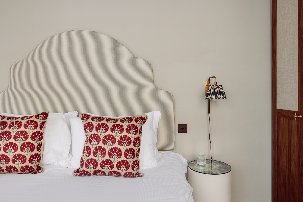 cream upholstered bedhead with red patterned cushions and fabric lampshade
