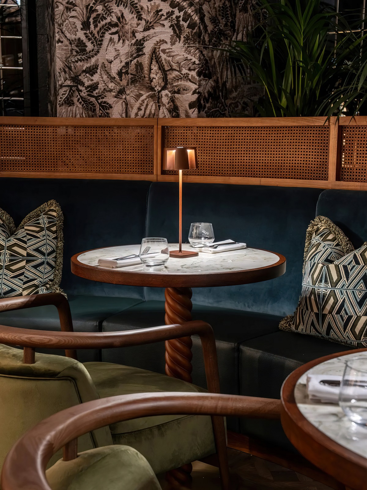 patterned cushions on blue banquette behind round wooden tables