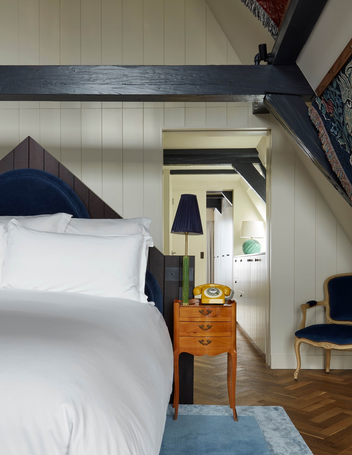 bed under beams with wooden panelled wall leading through to bathroom