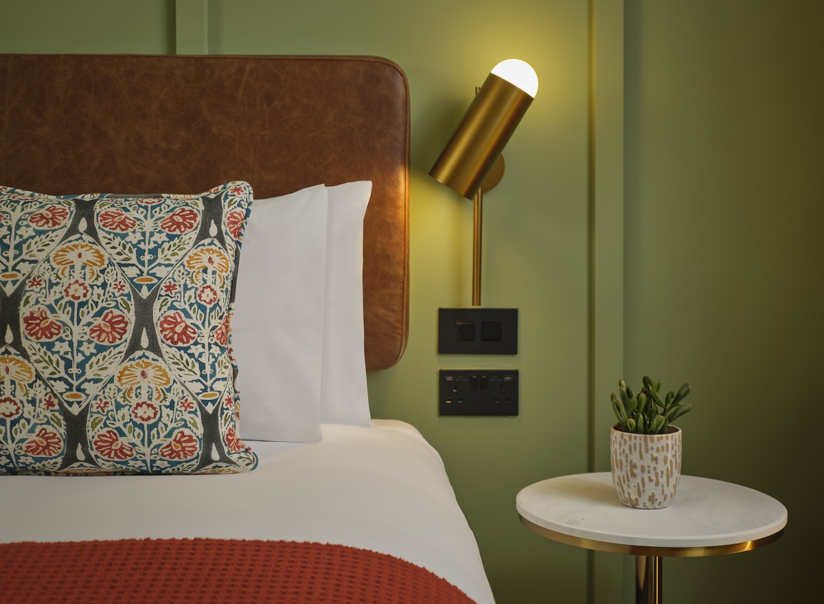 detail of green wall, headboard, patterned cushion and reading lamp in The Reach Manchester