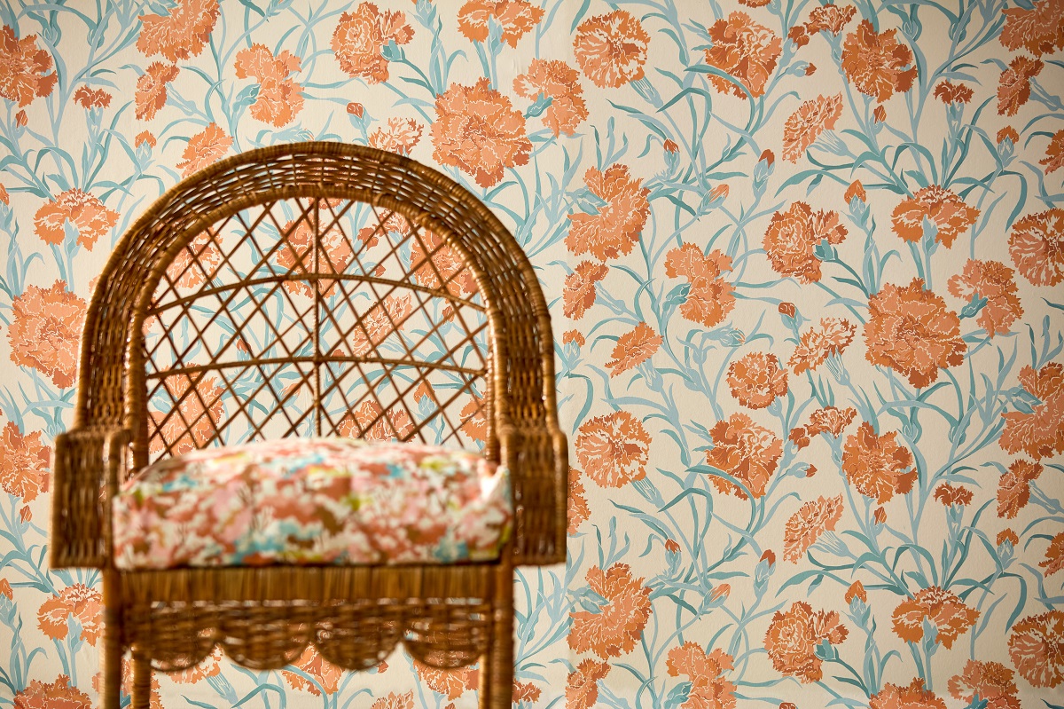 wicker chair with floral cushion set against floral wallpaper by Harlequin