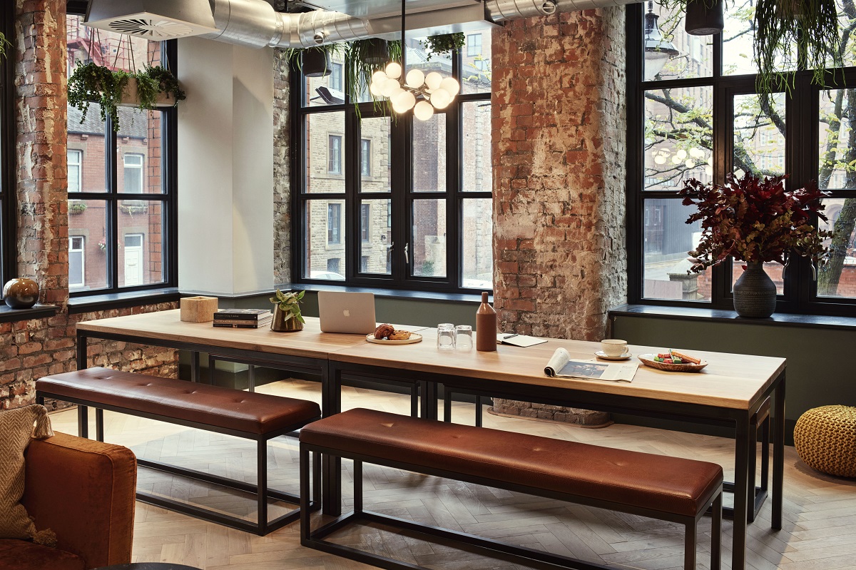 The dining room at LEVEN Manchester has a large communal dining table set within the iconic bare-brick walls of the hotel