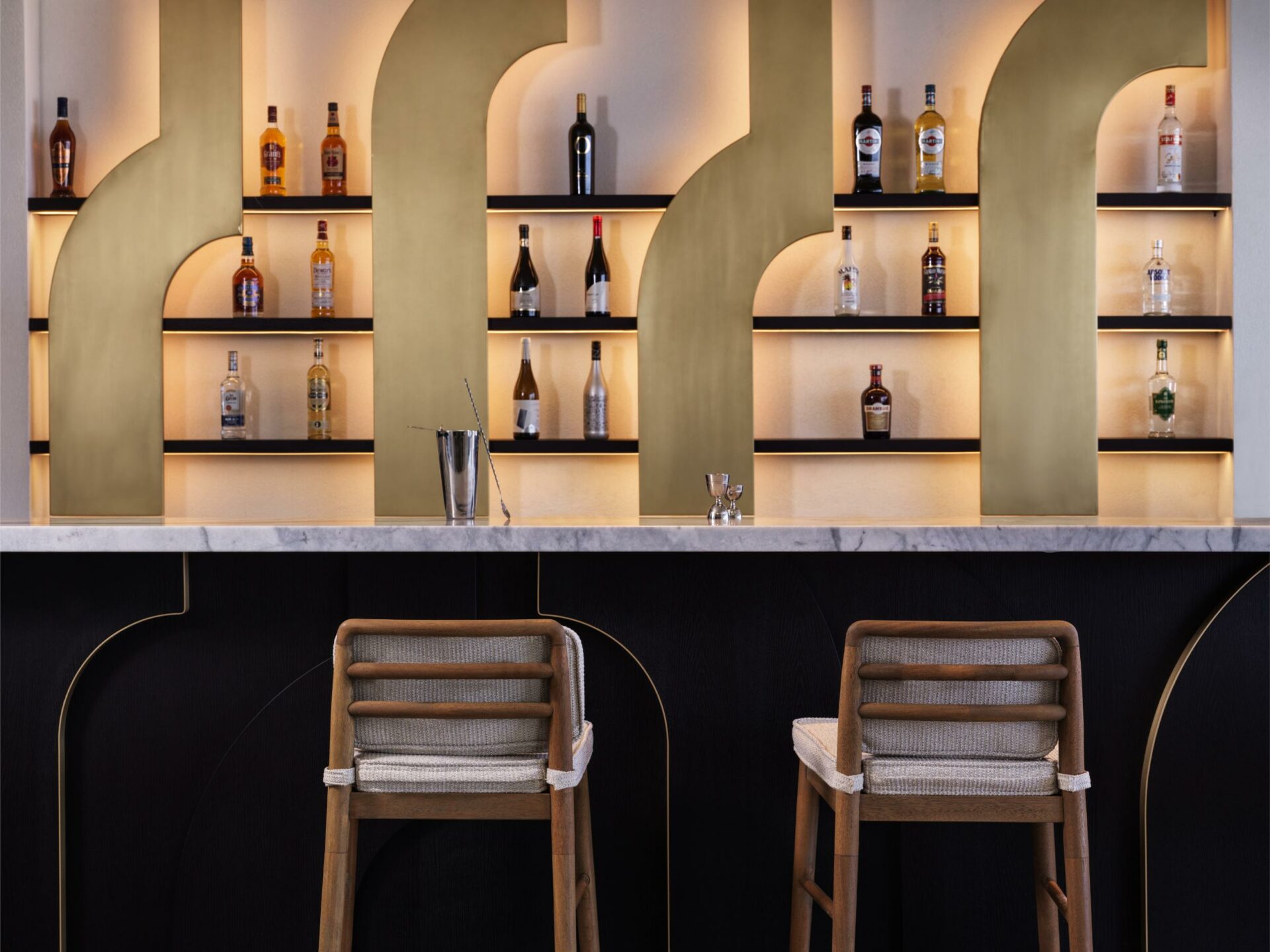 two wooden barstools against wood bar front with cream plaster backlit bar