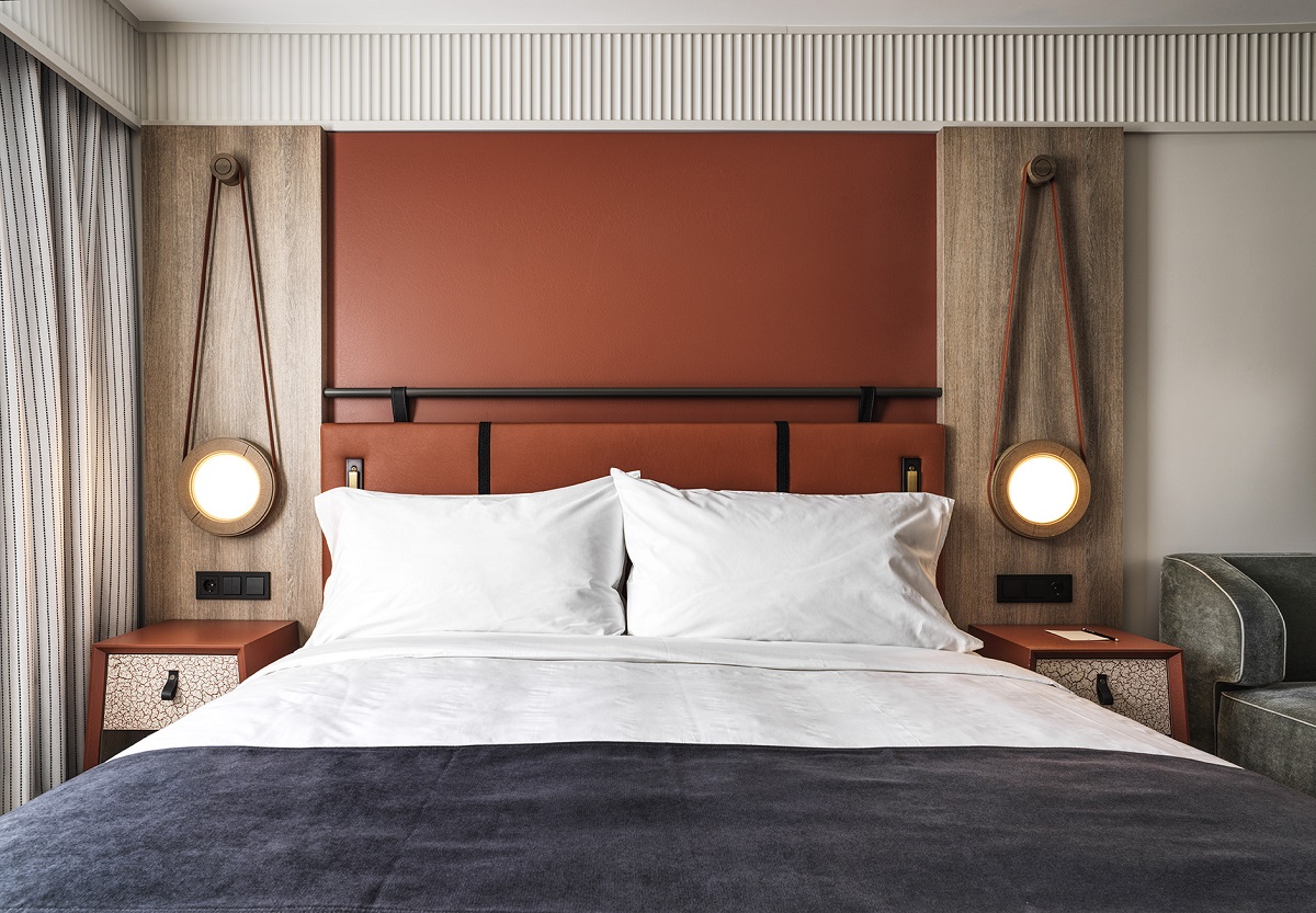 hotel guestroom with terracotta red wall behind the bed and leather detail bedside lights