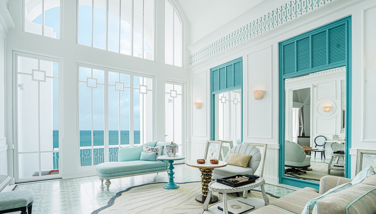 white chairs in front of floor to ceiling white framed windows in room with turquoise accents overlooking turquoise sea