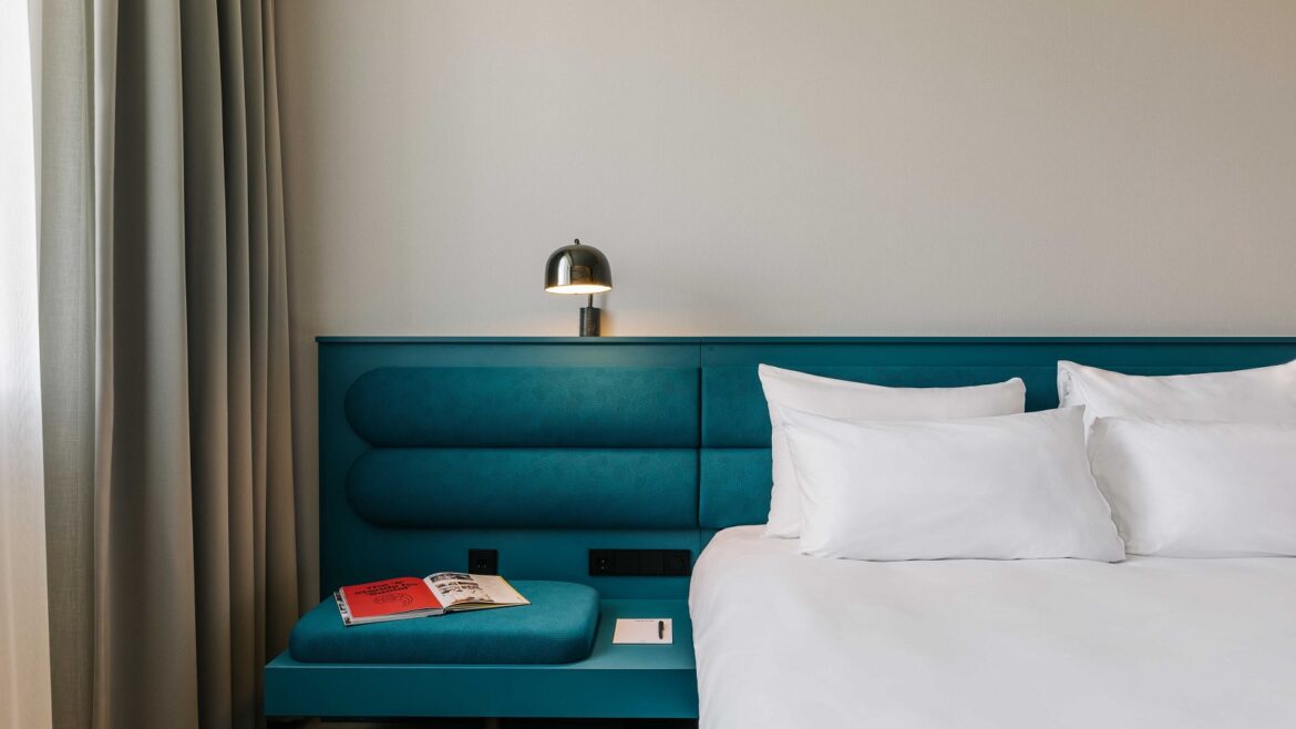 blue headboard and bed side table with book and light and white linen on bed