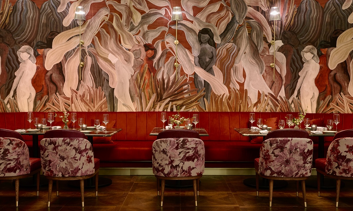 mural in red and brown on wall behind red banquettes