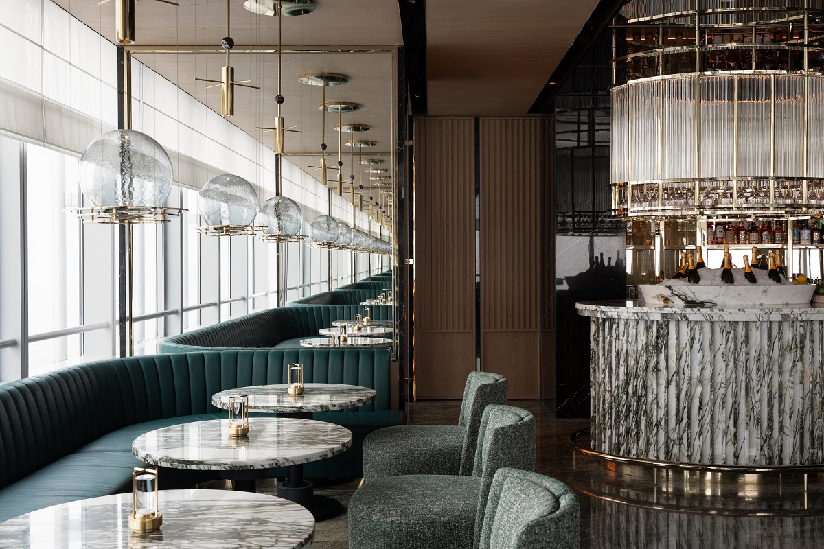 The bar area is flanked by sophisticated teal banquette seating and marble-topped tables