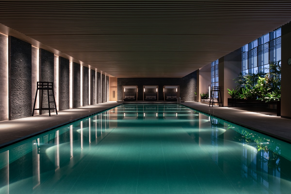 The pool area is lit with low-level atmospheric LEDs where stone walls and plantlife frame each side of the large pool.