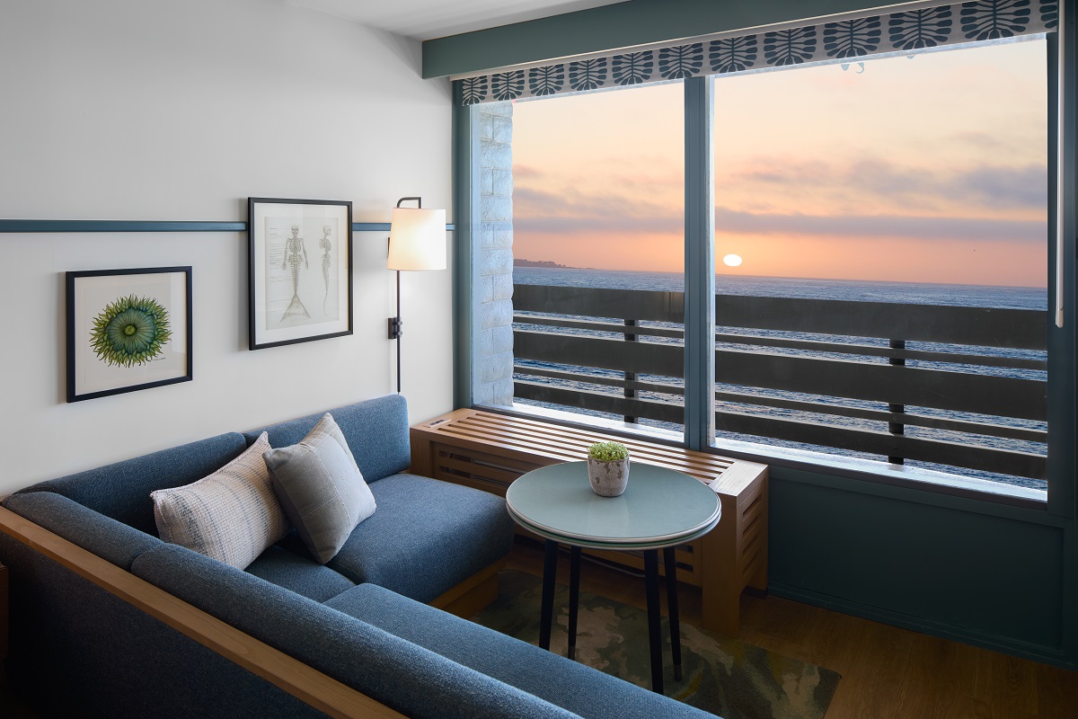 A blue corner sofa emulates the ocean views it sits opposite with large windows framing the sunset