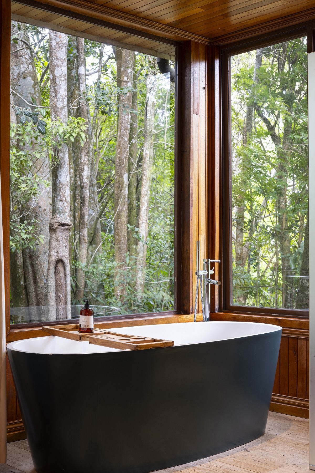 black freestanding bath with windows looking over treetops