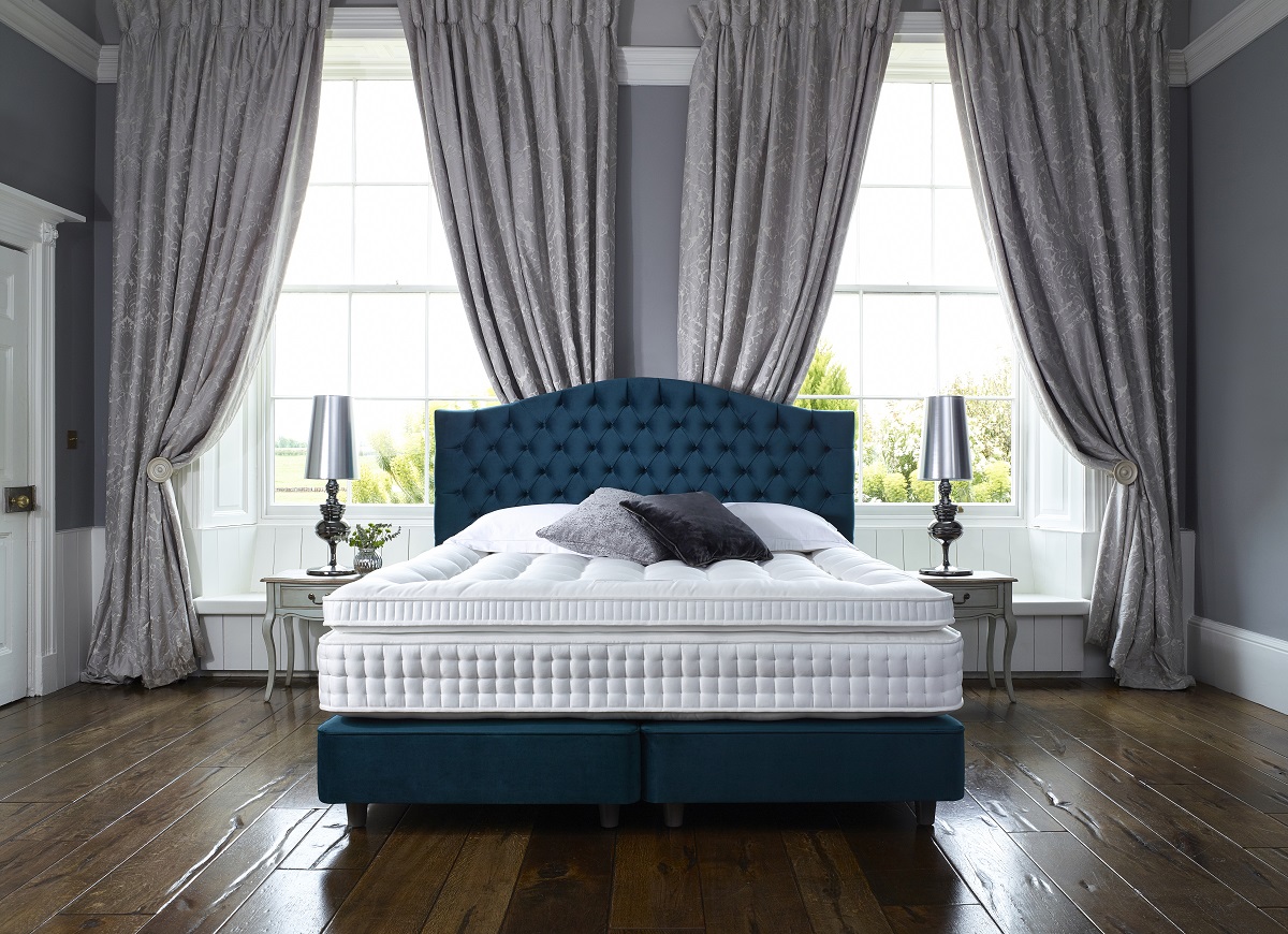 Bed with a blue headboard set against a window with gray folded curtains