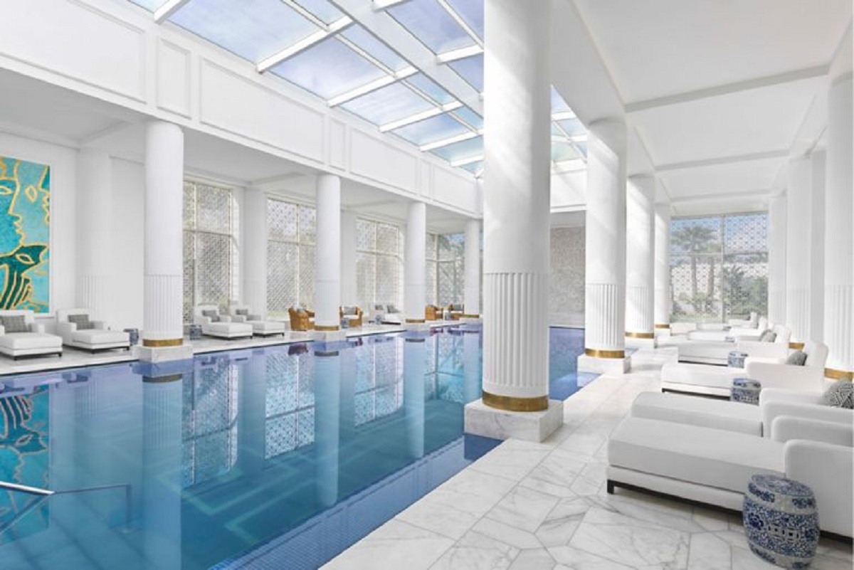 A large indoor pool area in the hotel surrounded by white columns and cabana daybeds